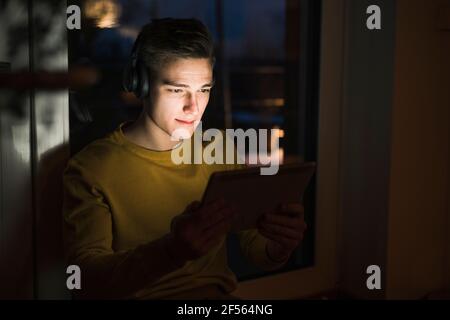 Junger Mann, der Kopfhörer trägt, während er Videos auf einem digitalen Tablet ansieht Im Wohnzimmer Stockfoto