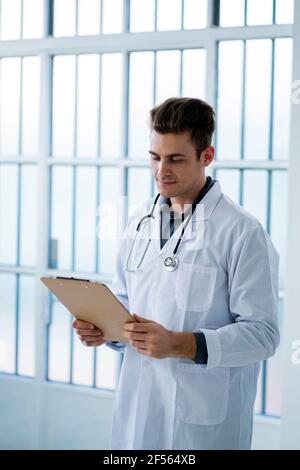 Männlicher Arzt, der Dokumente ansieht, während er die Zwischenablage im Krankenhaus hält Stockfoto
