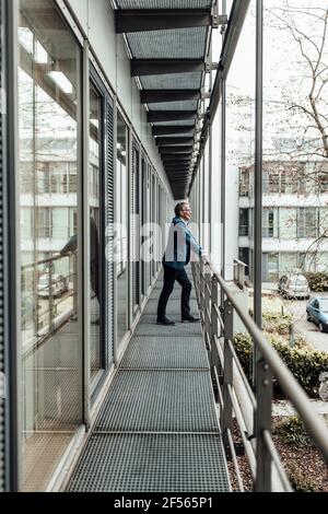 Der Geschäftsmann schaut weg, während er sich auf dem Bürobalkon auf das Geländer stützt Stockfoto