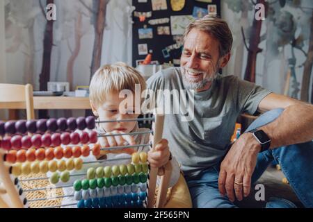 Glücklicher Vater beobachtete, wie der Sohn Abakus im Schlafzimmer zählte Stockfoto