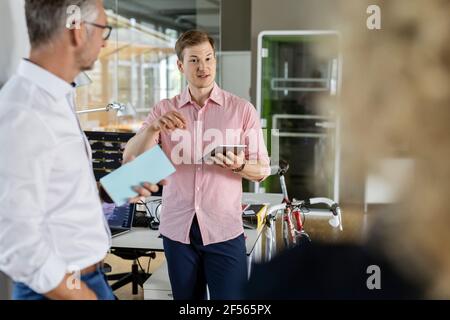 Junger Geschäftsmann mit digitalem Tablet, der Kollegen im Büro die Pläne erklärt Stockfoto