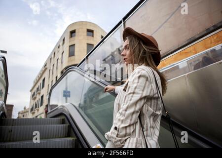 Frau mit Hut, der auf der Rolltreppe steht, während sie wegschaut Stockfoto