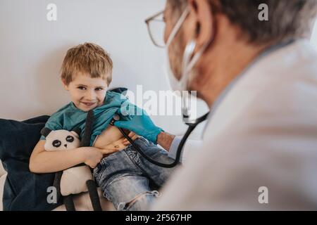 Kinderarzt untersucht lächelnden Jungen mit Stethoskop in der Klinik Stockfoto