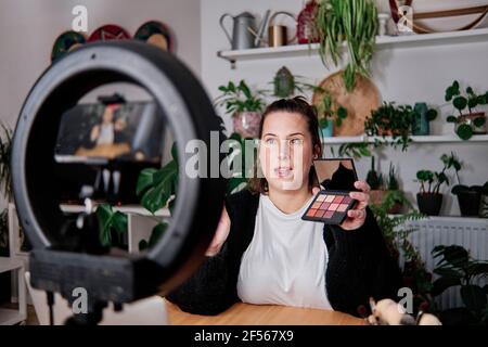 Weibliche Vlogger zeigt Beauty-Produkt während der Aufnahme Make-up-Tutorial bei Zu Hause Stockfoto