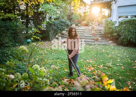 Fröhliche Frau, weitläufiger Garten mit Besen im Hinterhof Stockfoto