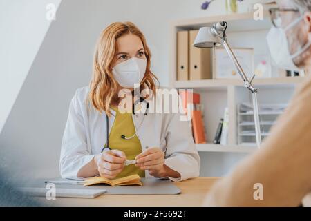 Allgemeinpraktikerin diskutiert über Impfpass mit Patient bei Büro Stockfoto