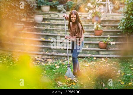 Lächelnde Frau, die im Garten mit Rechen fegen Stockfoto