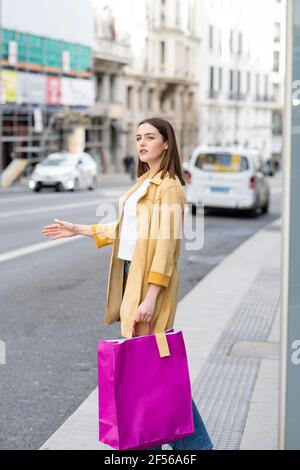 Frau mit Einkaufstaschen, die ein Taxi anhagelt, während sie auf dem Bürgersteig steht Stockfoto