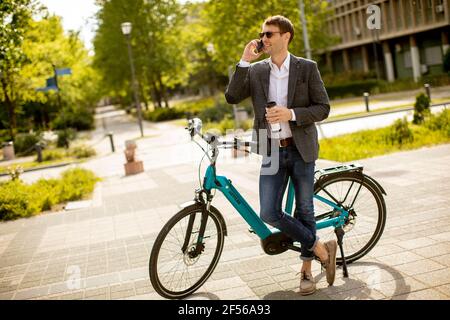 Schöner junger Geschäftsmann mit Handy von der eBike mit Kaffeetasse zum Mitnehmen Stockfoto