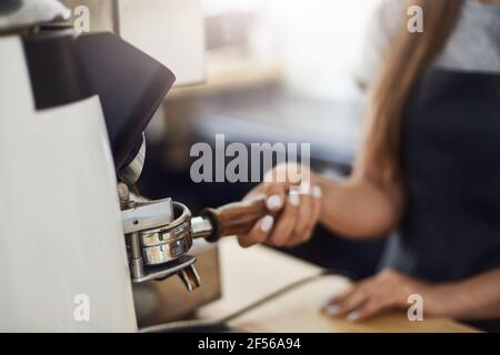 Nahaufnahme von Barista, der Kaffeemühle verwendet, um einen zu füllen Portafilter Stockfoto