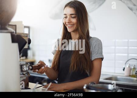 Junge Barista Student mit einer Kaffeemühle zu mahlen Bohnen in einen Portafilter Stockfoto