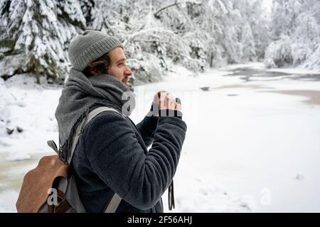 Junger Mann mit Rucksack und Kamera schaut im Stehen weg Im Wald Stockfoto