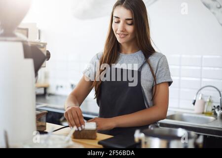 Portrait von jungen und niedlichen Barista Praktikantin kümmert sich um ihren Arbeitsplatz Reinigung alles mit einem Pinsel. Stockfoto