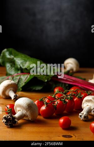 Rote Kirschtomaten mit essbaren Pilzen und Mangold auf Holztisch Stockfoto