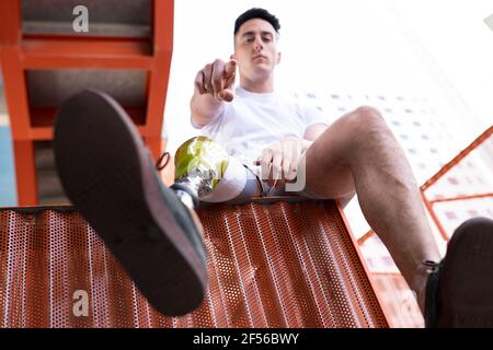 Amputierte junge Mann zeigt, während er auf Metall sitzt Stockfoto