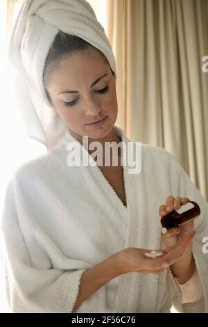 Junge Frau im Bademantel, die zu Hause Medizin nimmt Stockfoto