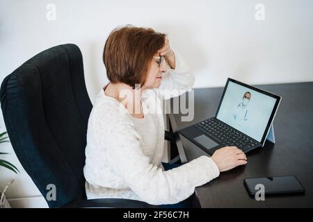 Frau, die an Kopfschmerzen leidet und vom Arzt auf Video beraten wird Anruf über Laptop zu Hause Stockfoto
