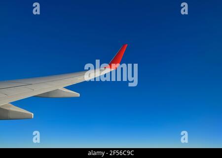 Flügel eines Verkehrsflugzeugs, das gegen den klaren blauen Himmel fliegt Stockfoto
