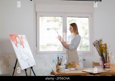 Künstlerin, die während des Fotografierens mit dem Smartphone fotografiert Im Studio zu Hause stehen Stockfoto