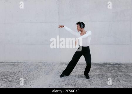 Flexibler Mann mit Kopfhörern, der an der weißen Wand tanzt Stockfoto