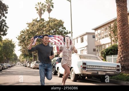 Junge Männer und Frauen laufen mit amerikanischer Flagge auf der Straße Stockfoto