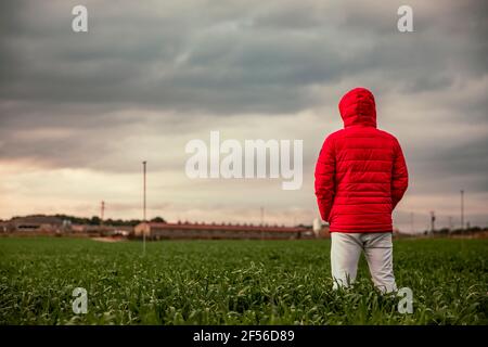 Kaukasischer Mann mit Wintermantel, der auf dem Feld gegen Wolken steht Himmel Stockfoto