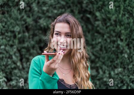Fröhliche Frau, die lachte, als sie Voicemail über das Mobiltelefon schickte parken Stockfoto