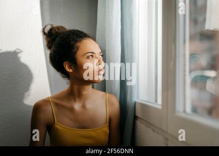 Nachdenkliche junge Frau Blick durch Fenster zu Hause Stockfoto