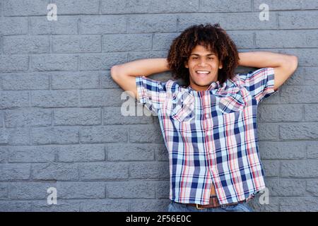 Portrait von jungen gemischten Renner lächelnd mit Händen hinter Kopf gegen graue Wand Stockfoto