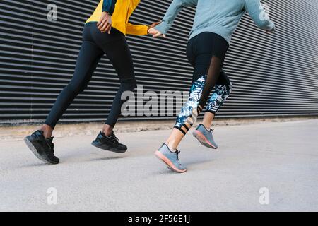 Eine Athletin und ein Athlet, die gemeinsam auf dem Bürgersteig an der Wand laufen Stockfoto