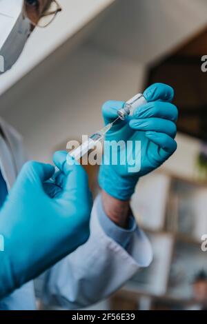 Arzt trägt Schutzhandschuh, der die COVID-19-Dosis-Spritze vorbereitet, während er am ist Klinik Stockfoto