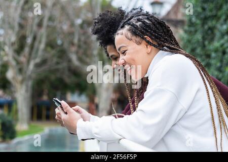 Lächelnde Frau mit Mobiltelefon, während sie bei Jungen im Freien steht Stockfoto