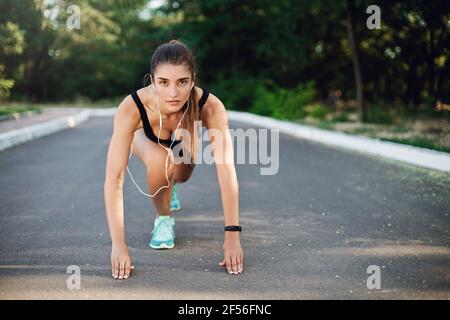 Sport, Fitness und urbanes Lifestyle-Konzept. Motivierte gut aussehende Frau führen ein aktives Leben, tun Morgenlauf, Sprinter stehen niedrigen Start auf Beton Stockfoto
