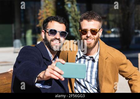 Lächelnde Geschäftspartner, die während des Sitzens Selfie über das Mobiltelefon machen Im Freien Stockfoto