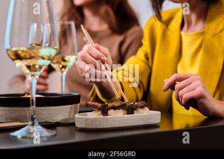 Frau, die frisches Sushi mit Essstäbchen isst, während sie bei einer Frau sitzt Freund im Restaurant Stockfoto