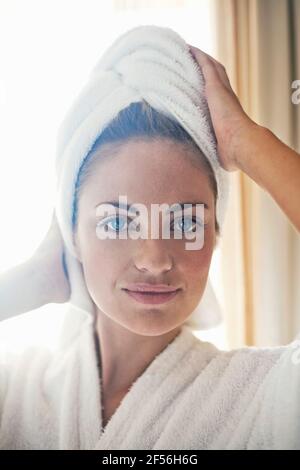 Lächelnde Frau trägt Bademantel und Handtuch um ihr Haar Zu Hause Stockfoto