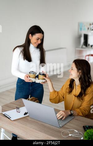 Lächelnde Tochter, die Mutter, die zu Hause arbeitet, Kaffee serviert Stockfoto