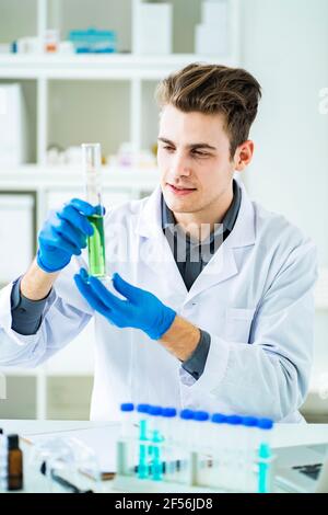 Hübscher Wissenschaftler, der Flüssigkeit im Zylinder untersucht, während er in arbeitet Labor Stockfoto