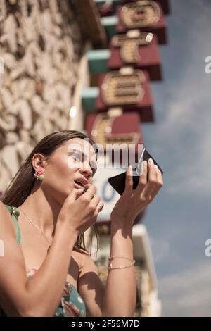 Junge Frau, die Lippenstift anklebt, während sie in den Palettenspiegel schaut Stockfoto