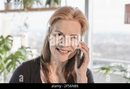 Schöne lächelnde Frau mit braunem Haar, die auf dem Handy spricht In Loft-Wohnung zu Hause Stockfoto