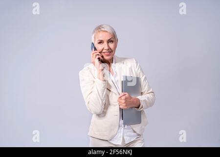 Lächelnde Geschäftsfrau, die auf dem Mobiltelefon spricht, während sie gegen Grau steht Hintergrund Stockfoto
