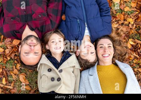 Familie lächelt, während sie sich auf einem gefallenen Blatt im Wald ausruhen Herbst Stockfoto