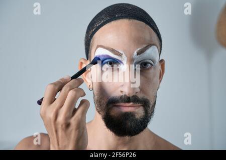 Mittelerwachsener Mann, der blauen Lidschatten mit Make-up-Pinsel aufführt Auge Stockfoto