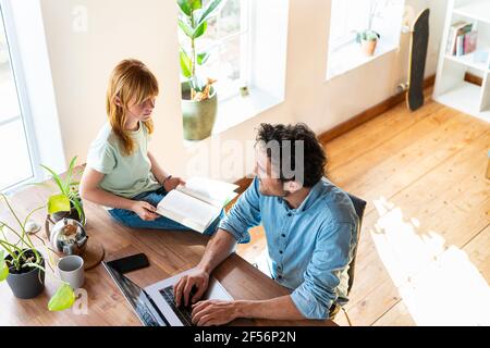 Rotschopf Mädchen mit Buch Blick auf Vater arbeiten von zu Hause aus Auf einem Laptop Stockfoto