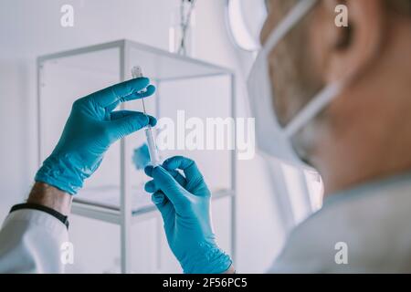 Arzt, der im Untersuchungsraum stehend eine Impfung in einer Spritze einnahm Während der COVID-19 Stockfoto