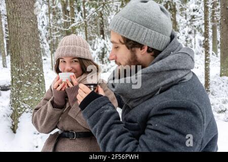 Paar trinken Kaffee, während sie im Winter im Wald sitzen Stockfoto