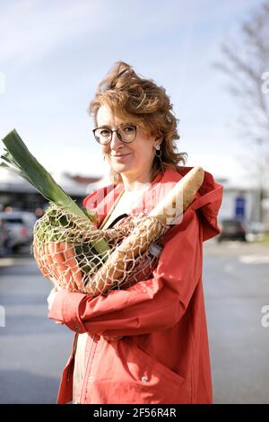 Lächelnde Frau, die im Freien stehend einen Netzbeutel mit Lebensmitteln hält Stockfoto