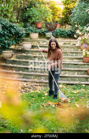 Frau in warmer Kleidung, die mit Rechen im Hinterhof fegen Garten Stockfoto