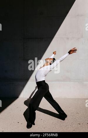 Männlicher Tänzer, der an einem sonnigen Tag gegen die Wand trainiert Stockfoto