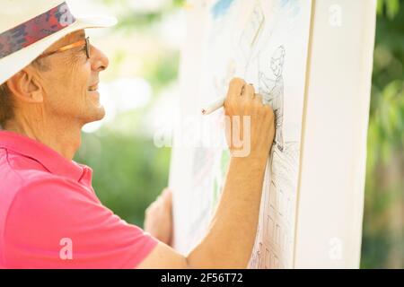 Senior Mann Zeichnung auf Leinwand im Garten Stockfoto